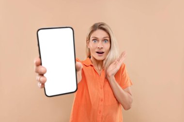 Elinde bej arka planda boş ekranlı akıllı telefon tutan sürpriz bir kadın.
