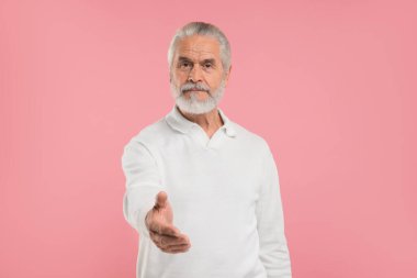 Kıdemli adam hoş geldin diyor ve pembe arka planda el sıkışma teklif ediyor.