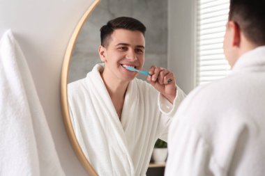Adam banyoda aynanın yanında diş fırçasıyla dişlerini fırçalıyor.
