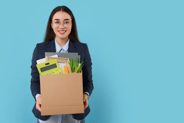 Happy unemployed woman with box of personal office belongings on light blue background, space for text