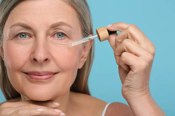 Seniorin Trägt Kosmetikprodukt Auf Ihre Alternde Haut Vor Hellblauem Hintergrund — Stockfoto