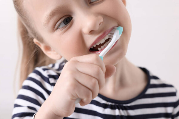Little girl brushing her teeth with plastic toothbrush on white background, closeup