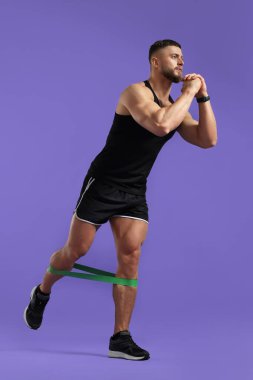 Mor arka planda elastik direnç bandıyla egzersiz yapan kaslı adam.