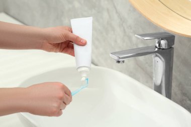 Banyoda lavabonun yanındaki diş fırçasına diş macunu sıkan bir kadın.