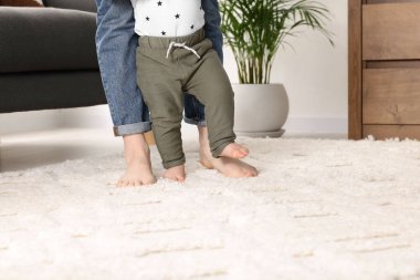 Anne, bebeğine evde halıda yürümeyi öğrenirken destek oluyor.
