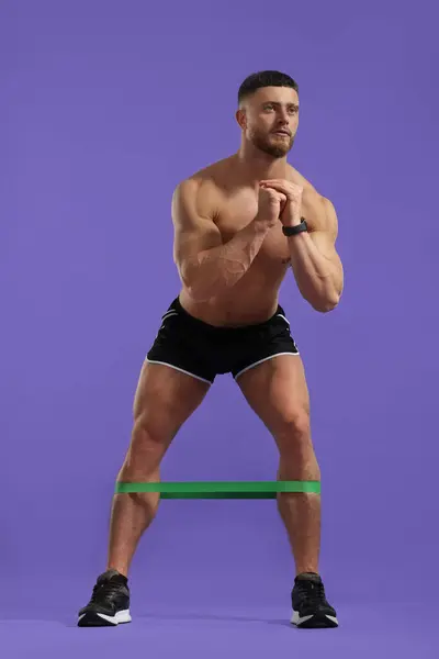 Muskularny Mężczyzna Ćwiczący Elastyczną Taśmą Oporową Fioletowym Tle — Zdjęcie stockowe