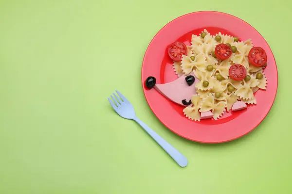 Creative serving for kids. Plate with cute hedgehog made of delicious pasta, sausages and tomatoes on green table, flat lay. Space for text