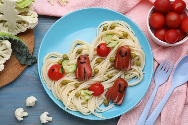 Creative serving for kids. Plate with cute octopuses made of sausages, pasta and vegetables on light blue wooden table, flat lay