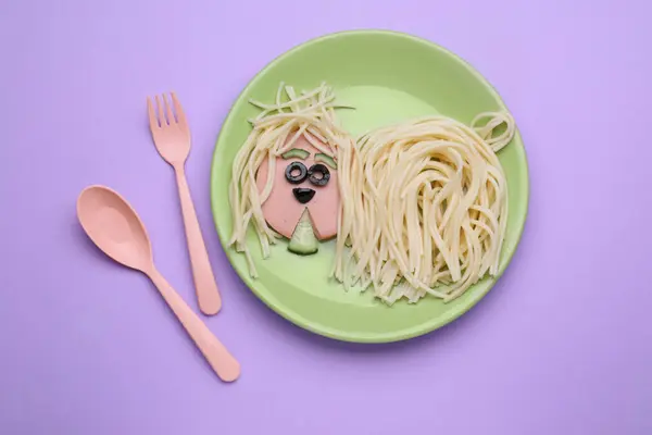 Creative serving for kids. Plate with cute dog made of tasty pasta, sausage and cucumber on violet table, flat lay
