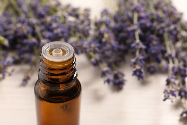 Bottle of essential oil and lavender flowers on white table, closeup. Space for text