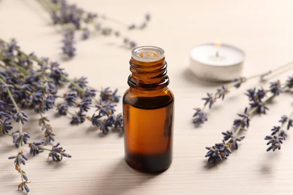 Bottle of essential oil and lavender flowers on white wooden table