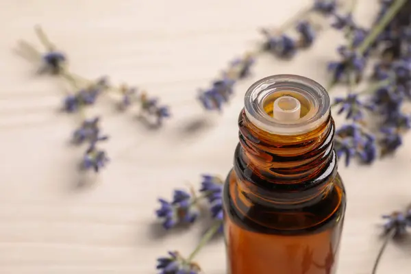 Bottle of essential oil and lavender flowers on white wooden table, closeup. Space for text