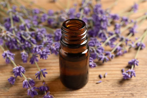 Bottle of essential oil and lavender flowers on table, closeup