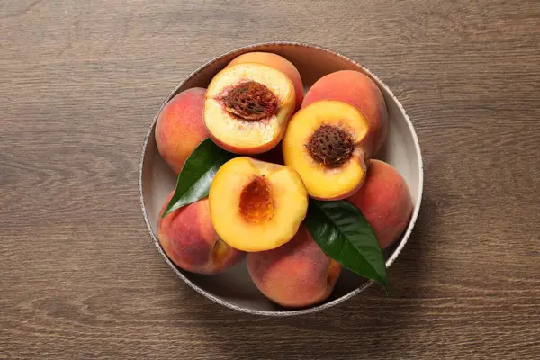 Plate with delicious juicy peaches and leaves on wooden table, top view