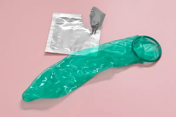 ピンクの背景に未登録のコンドームと引き裂かれたパッケージ 安全なセックス — ストック写真