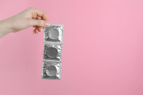 Женщина с презервативами на розовом фоне, крупным планом. Пространство для текста