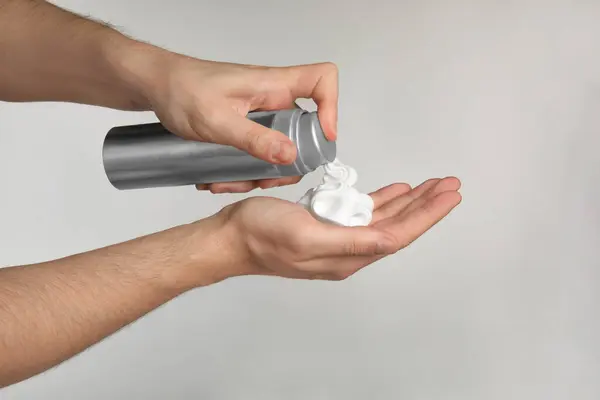 Man applying shaving foam onto hand on light grey background, closeup