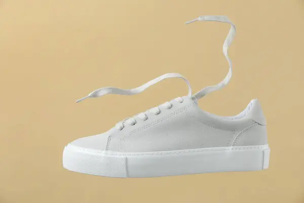 One stylish white sneaker on beige background