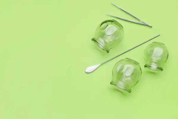 Glass cups, tweezers and torch on light green background, flat lay with space for text. Cupping therapy