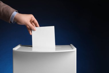 Kadın oyunu koyu mavi arka planda oy sandığına koyuyor, yakın plan. Metin için boşluk