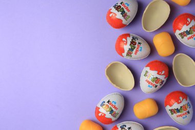 Sveti Vlas, Bulgaristan - 29 Haziran 2023: Mor arka planda Kinder Sürpriz Yumurtalar ve plastik kapsüller, düz konum. Metin için boşluk