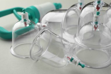 Plastik bardaklar ve el pompası açık gri arka planda, yakın plan. Fincan terapisi.