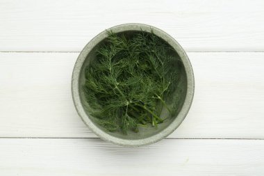 Beyaz ahşap masa üzerinde taze yeşil dereotu kasesi.