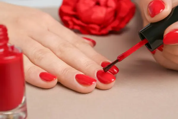 Woman painting nails with red polish on beige background, closeup