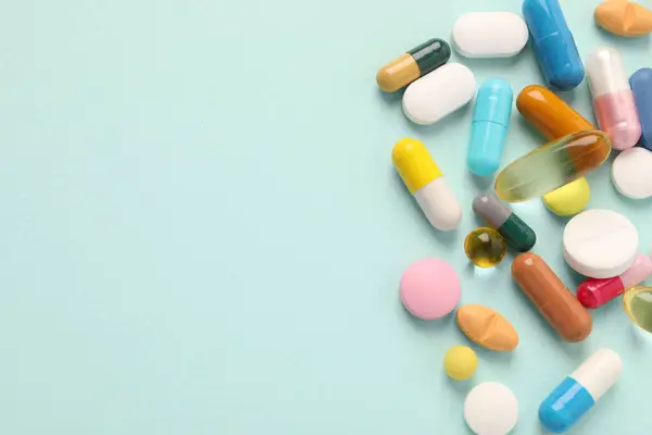 Pile of different pills on mint background, flat lay. Space for text