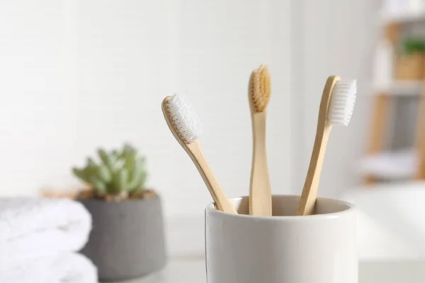 Bamboo toothbrushes in holder on blurred background, closeup. Space for text