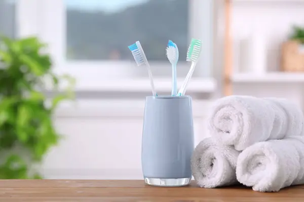 Plastic toothbrushes in holder and towels on wooden table. Space for text