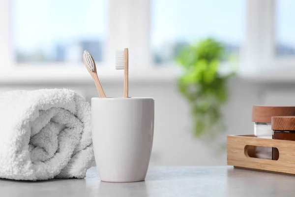 Bamboo toothbrushes in holder, towel and cosmetic products on light grey table indoors. Space for text