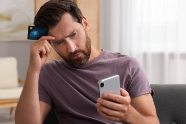 Kredi kartıyla evde akıllı telefon kullanan üzgün bir adam. Dikkatli ol, sahtekar.