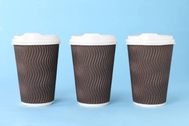 Açık mavi arka planda beyaz kapaklı kağıt bardaklar. Kahve hazır.