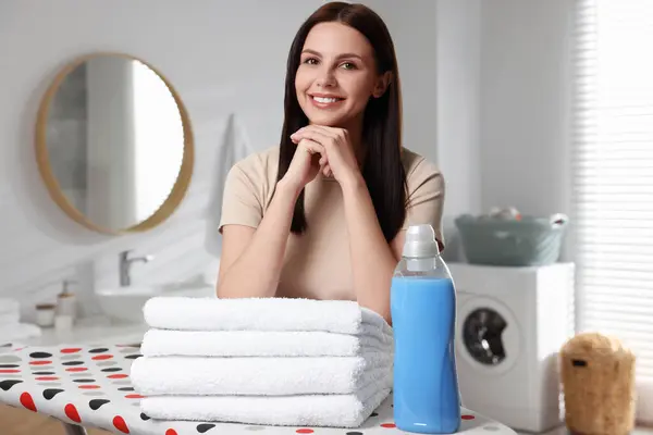 Woman near fabric softener and clean towels in bathroom