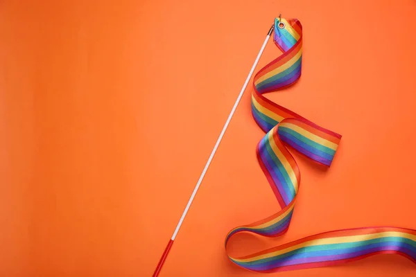 Stick with rainbow ribbon on orange background, top view and space for text. LGBT pride