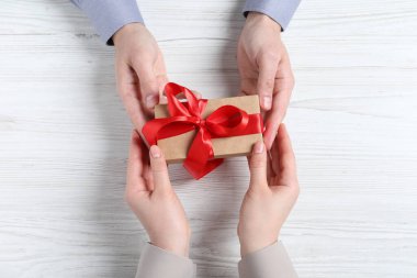 Beyaz ahşap masadaki kadına hediye paketi veren adam.