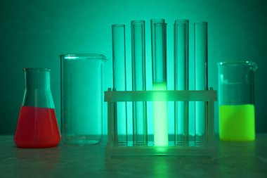 Yeşil arka planda parlak sıvılar bulunan laboratuvar camları.