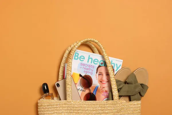 Flat lay composition with wicker bag and other beach accessories on orange background. Space for text