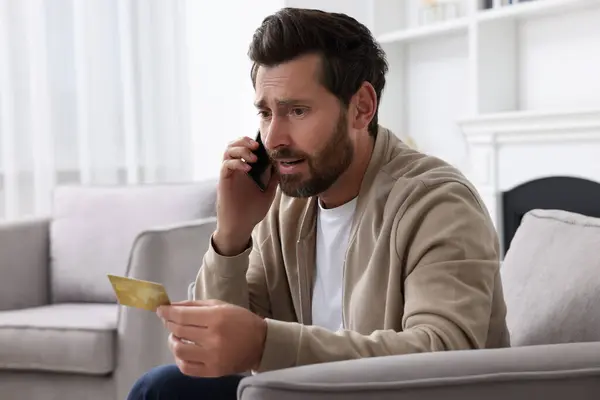 Zdenerwowany Człowiek Kartą Kredytową Rozmawiający Przez Telefon Fotelu Domu Uważaj — Zdjęcie stockowe