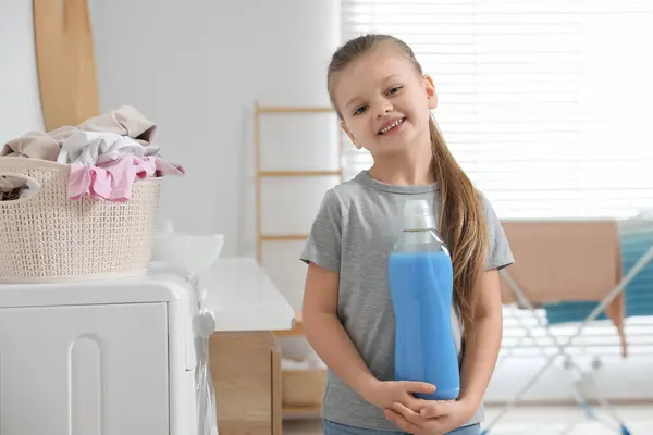 Little girl holding fabric softener in bathroom, space for text