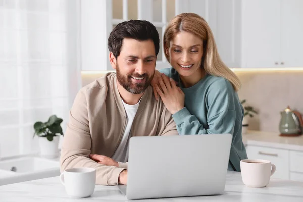 Happy couple with laptop at white table in kitchen