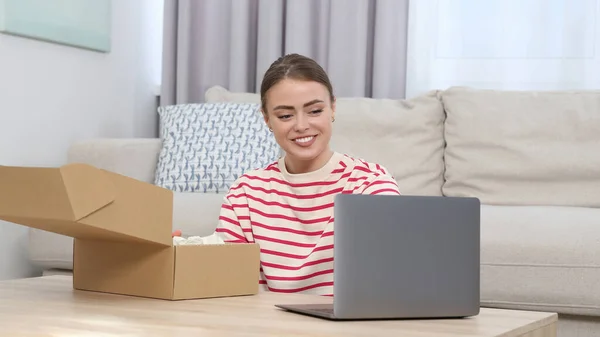 Happy woman with laptop unpacking parcel at home. Online store