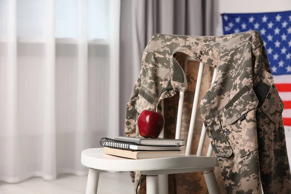 Chair with soldier uniform, notebooks and apple near flag of United States indoors, space for text. Military education