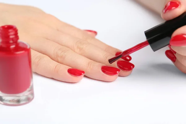Woman painting nails with red polish on white background, closeup