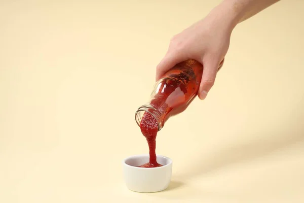 Vrouw Gieten Smakelijke Ketchup Uit Fles Kom Beige Achtergrond Close — Stockfoto