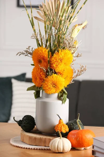 Beautiful bouquet with bright orange flowers and pumpkins on table indoors. Autumn vibes
