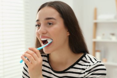 Banyoda dişlerini plastik diş fırçasıyla fırçalayan genç bir kadın.