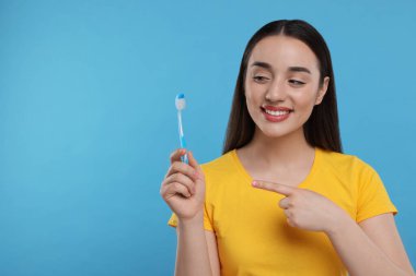 Açık mavi arka planda plastik diş fırçası tutan mutlu genç kadın, metin için boşluk