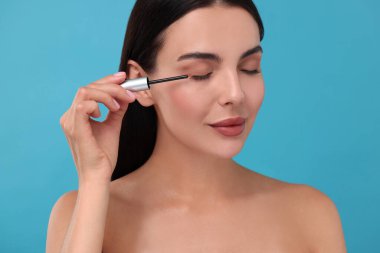 Kirpiklerine açık mavi arka planda serum süren güzel bir kadın. Kozmetik ürünü
